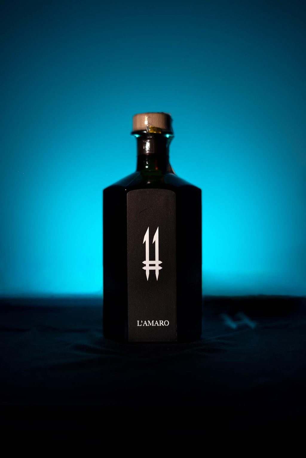 N.11 L'Amaro — L'Oscuro, bottiglia esagonale scura su fondo azzurro