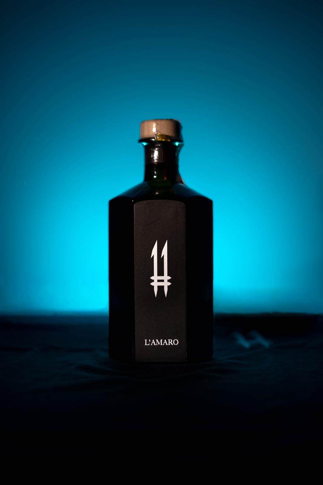 N.11 L'Amaro — L'Oscuro, bottiglia esagonale scura su fondo azzurro