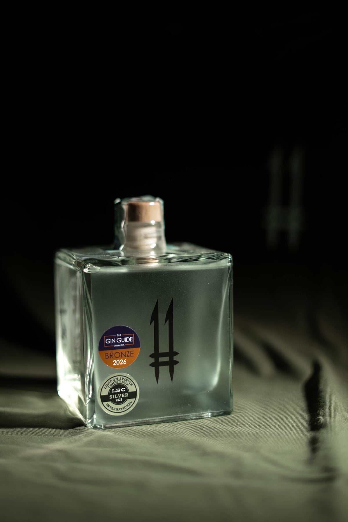 Bottiglia quadrata trasparente di N.11 London Dry Gin Il Guardiano con logo 11 nero e bollini dei premi 2026